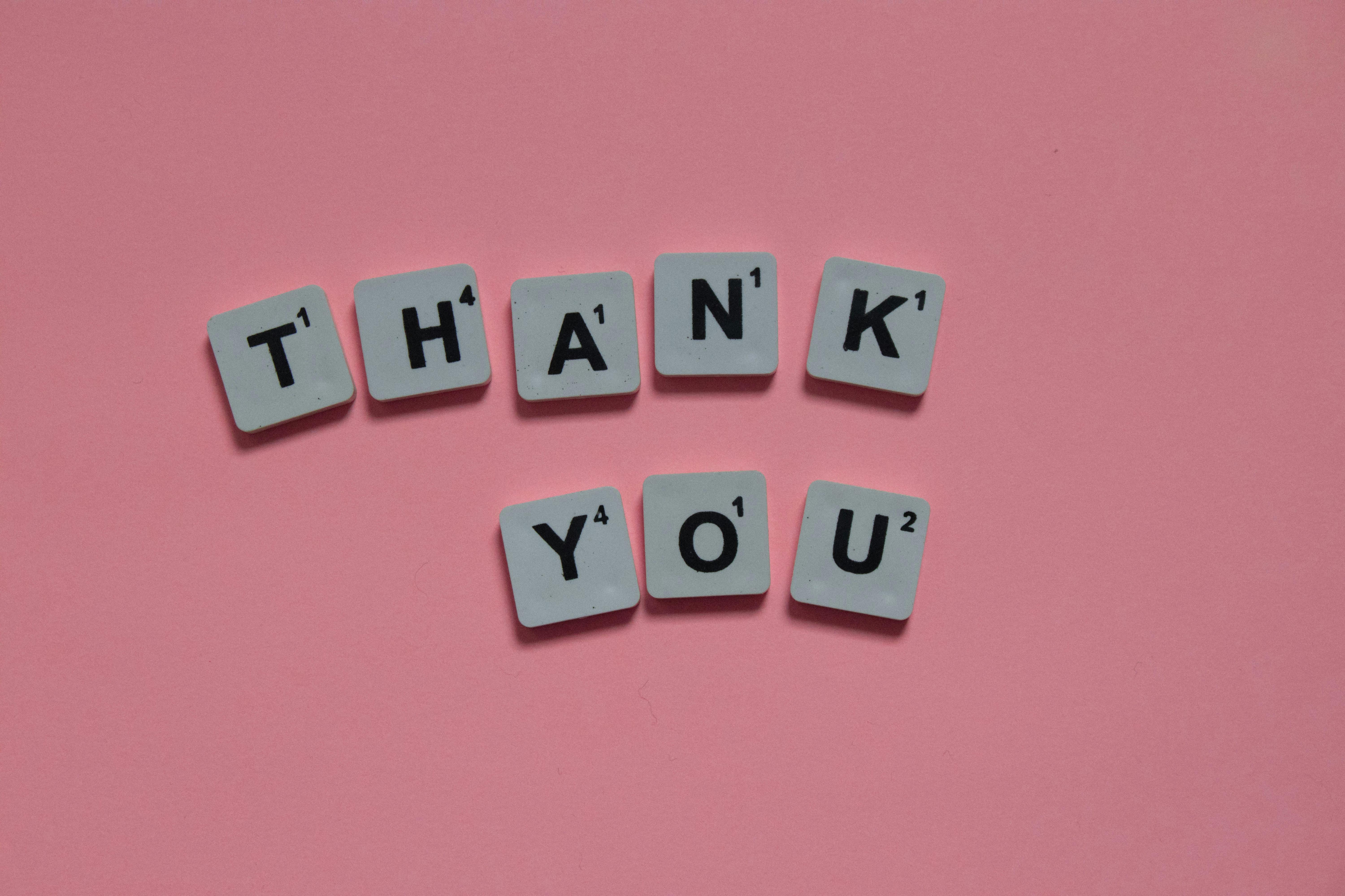 Scrabble tiles forming 'Thank You' on a pink background, ideal for gratitude concepts.