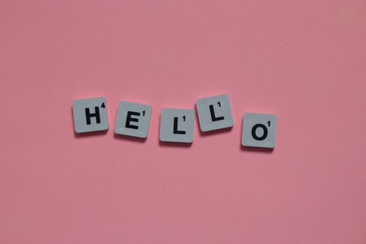 Scrabble tiles arranged to spell 'hello' on a soft pink background, with copy space.