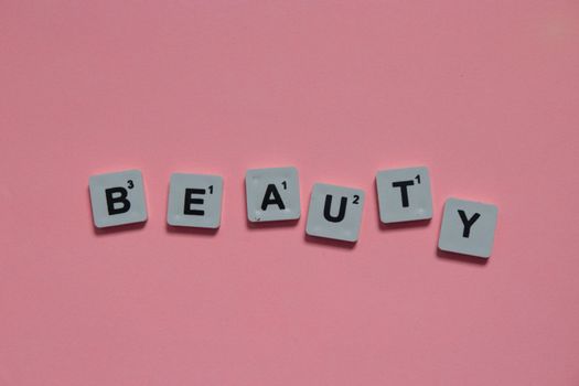 Scrabble tiles spelling 'beauty' on a pink background, symbolizing elegance.