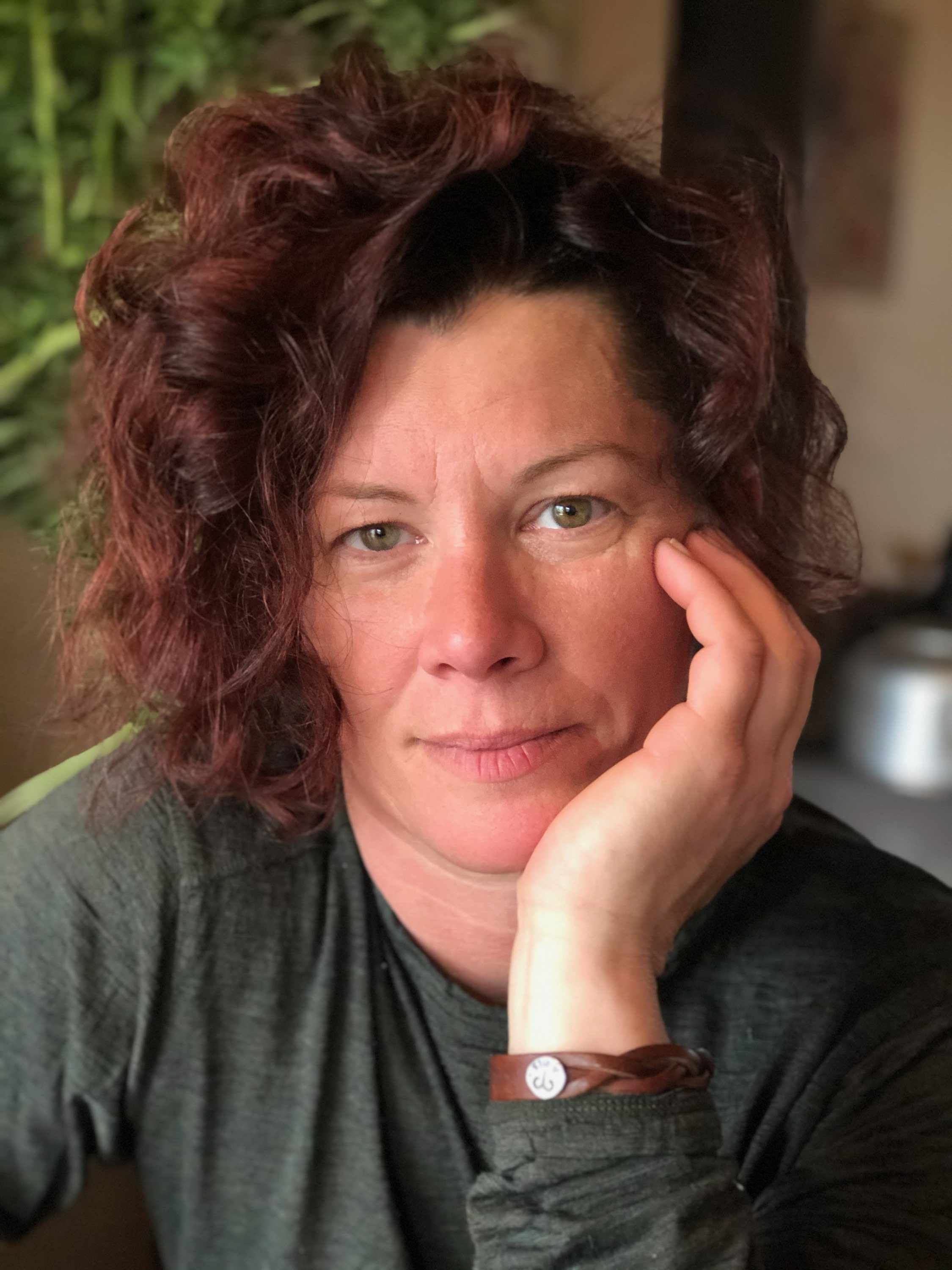 Portrait of a woman with curly hair, sitting indoors, looking thoughtful.