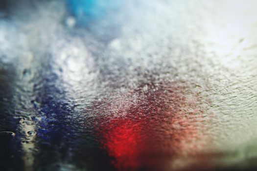 A colorful abstract image of water droplets on a glass surface with red and blue hues.
