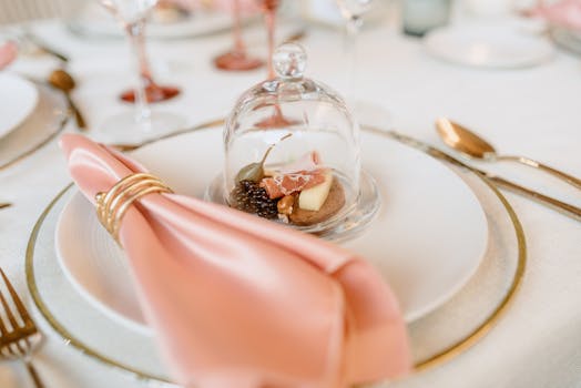 Luxe table setting featuring a cheese and nut platter under glass with a pink napkin.