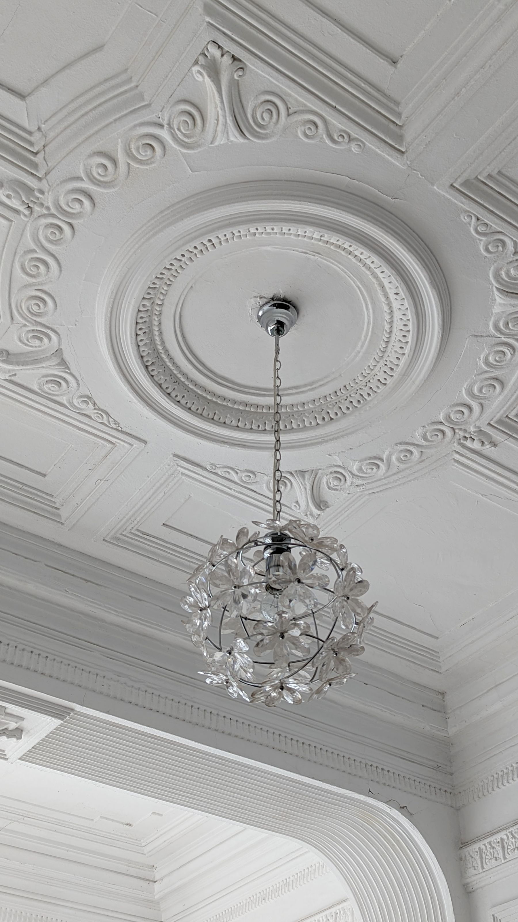 White ceiling rose and scrollwork plaster panels around a hanging floral light