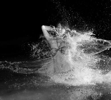 Engaging black and white photo of a woman experiencing a joyful splash at the beach.