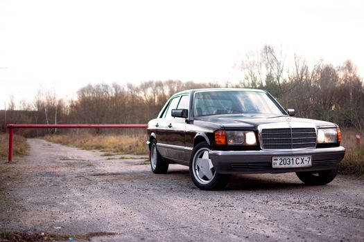 Vintage black sedan parked on a dirt road with autumn trees in the background.