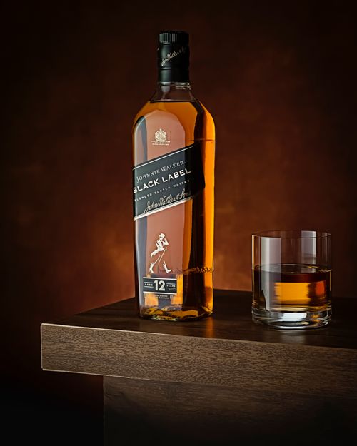 Free Luxurious whisky bottle next to a glass on a dark wooden surface, perfect for premium drink ads. Stock Photo