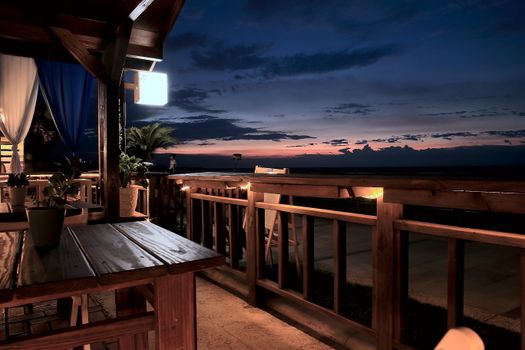 Serene outdoor patio overlooking the ocean at twilight with wooden furniture and gentle ambient lighting.