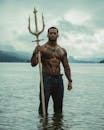 一名打扮成水上超级英雄的男子自信地在水中摆出姿势，手持三叉戟，体现了力量和神话