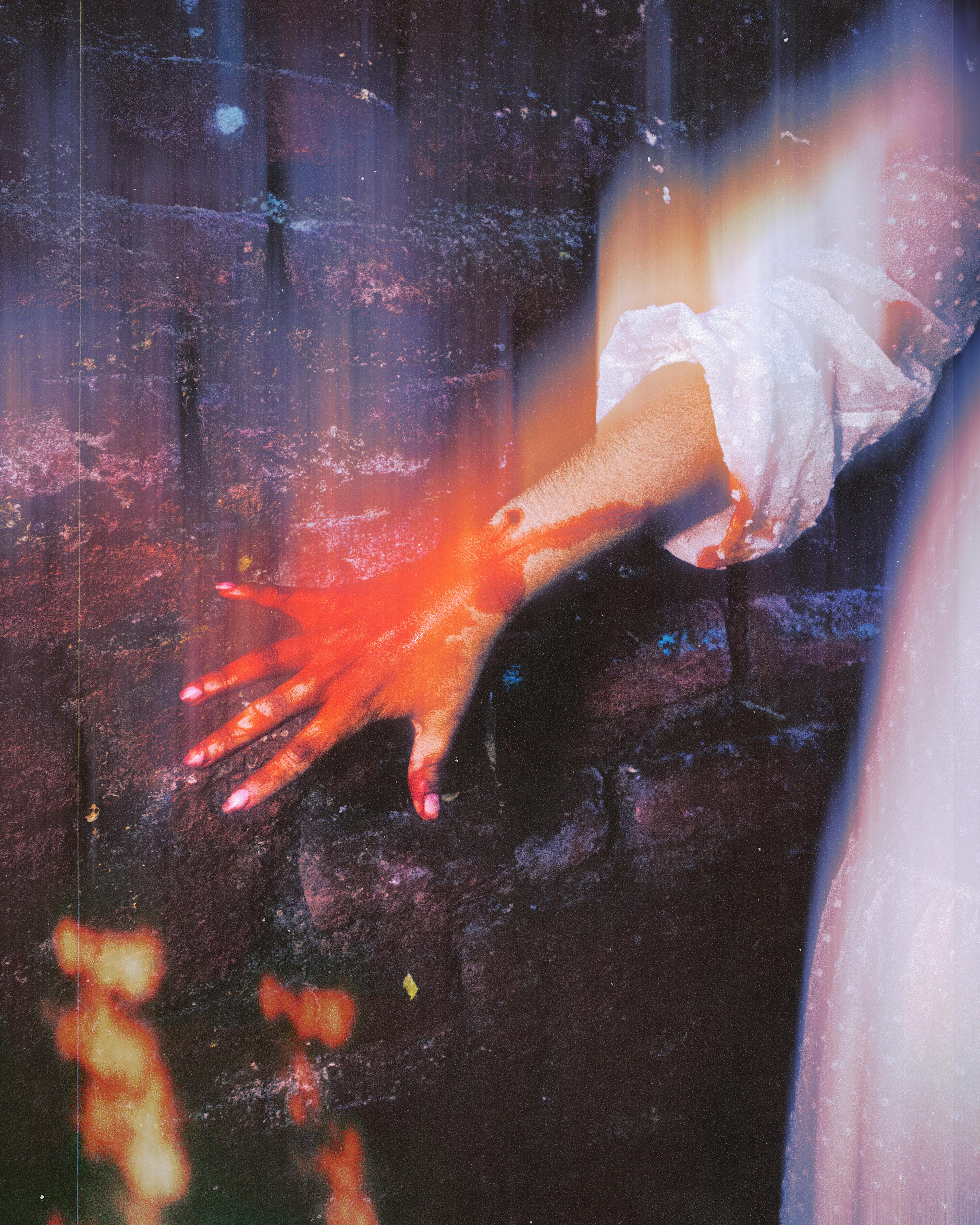 Artistic portrayal of a woman's hand touching a textured brick wall with a surreal glow effect.