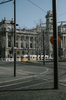 A serene view of a tram passing by a historic building in Budapest, featuring architectural charm and urban tranquility.
