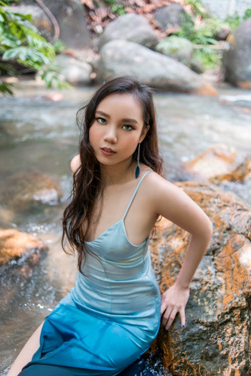 A beautiful young woman in a blue dress sitting on rocks