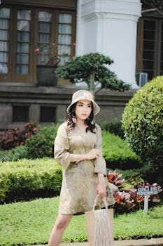 Elegant woman in a hat and floral dress posing outdoors in Bandung garden.
