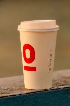 A disposable coffee cup with a red design against a blurred background, perfect for lifestyle themes.
