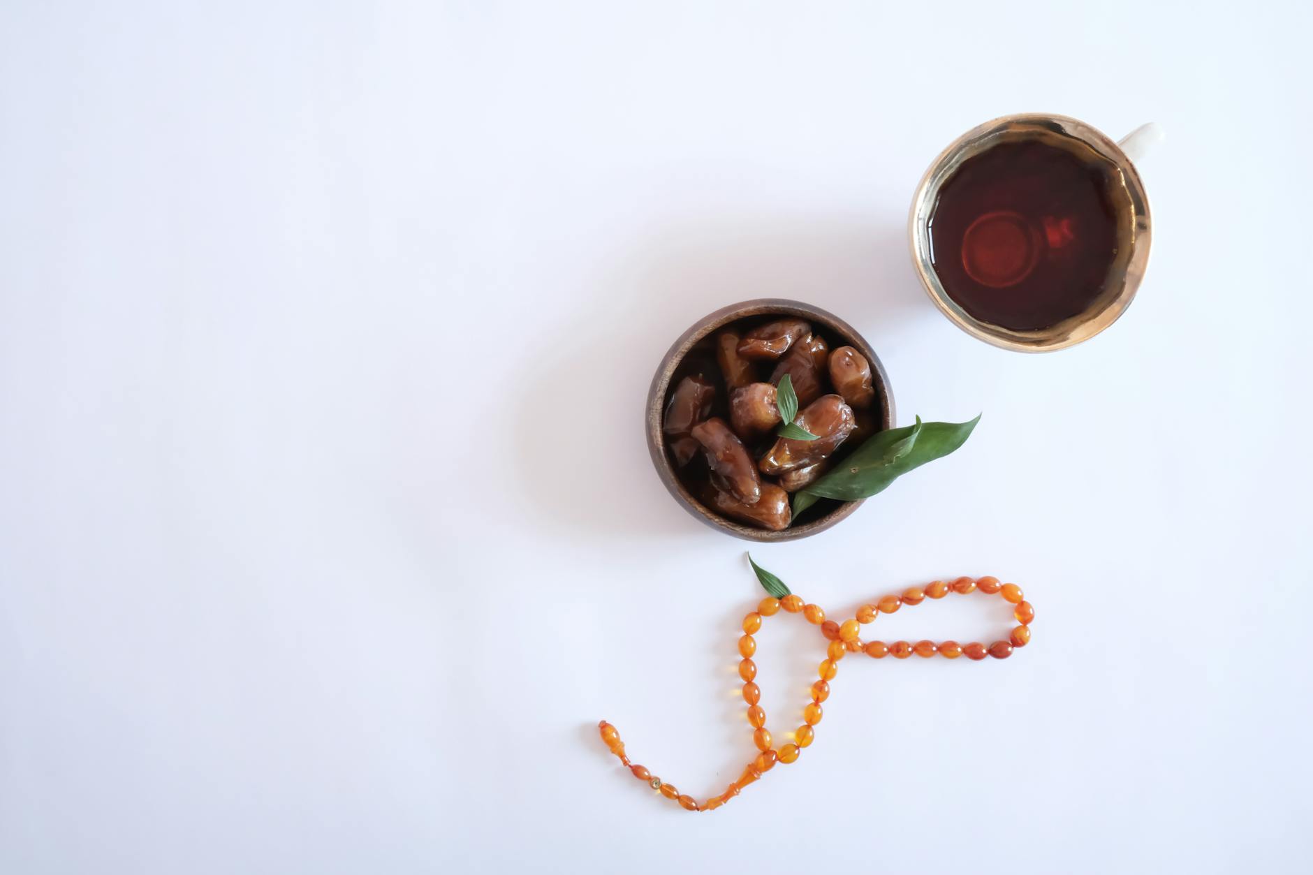 Overhead view of Ramadan iftar with dates, tea, and prayer beads on a white background.