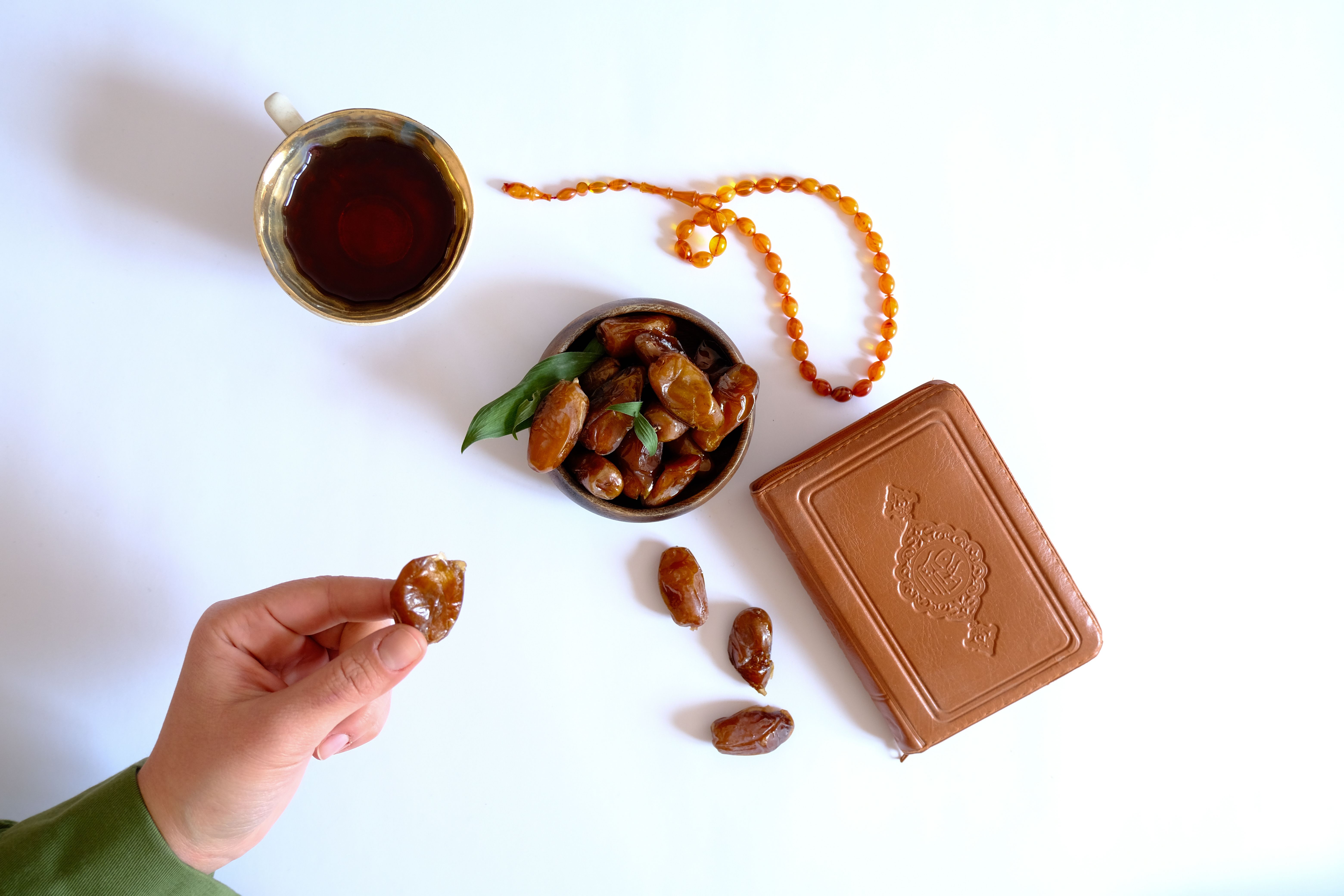 A serene flat lay depicting a cup of tea, dates, amber prayer beads, and a leather-bound book.