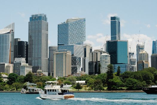 Modern Sydney skyline with vibrant blue skies, skyscrapers, and boats on the harbor.