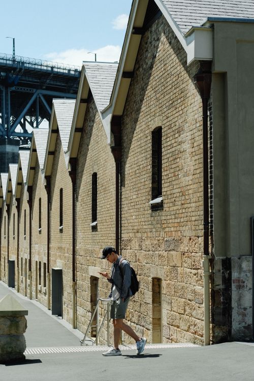 Free Man walking along historic warehouses in Sydney, showcasing urban architecture. Stock Photo
