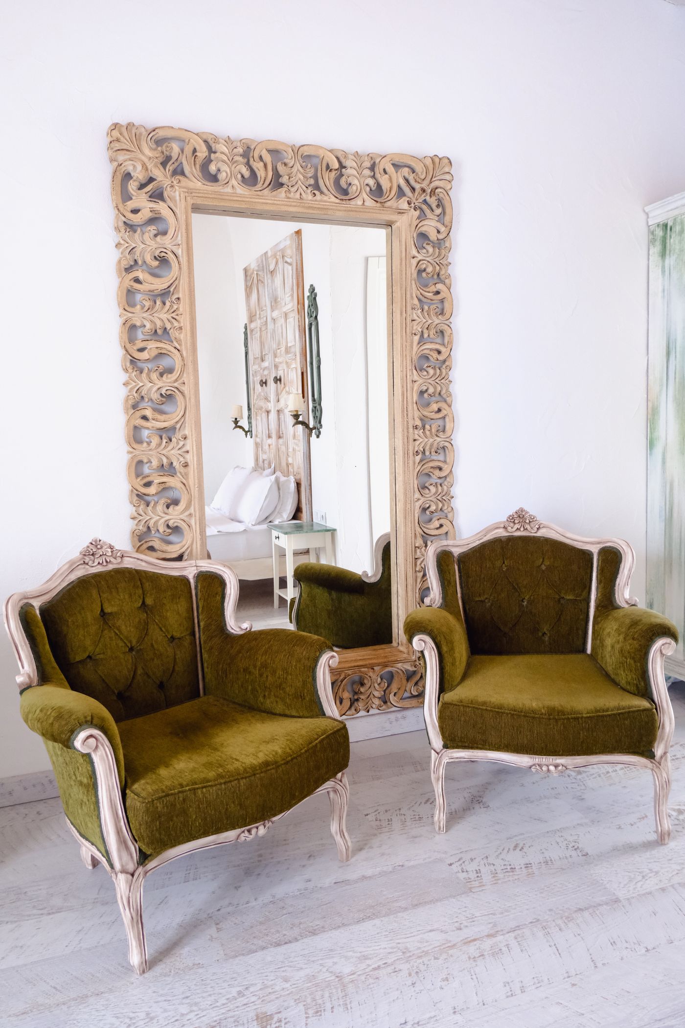 A pair of antique olive-green armchairs beside an ornate gilt mirror