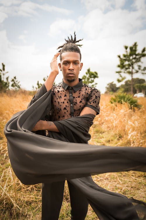 Man with Dreadlocks Wearing a Black Outfit and Posing on a Dry Grass Field 