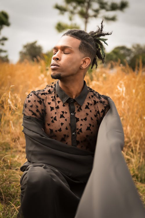 Man with Dreadlocks Wearing a Black Outfit and Posing on a Dry Grass Field 