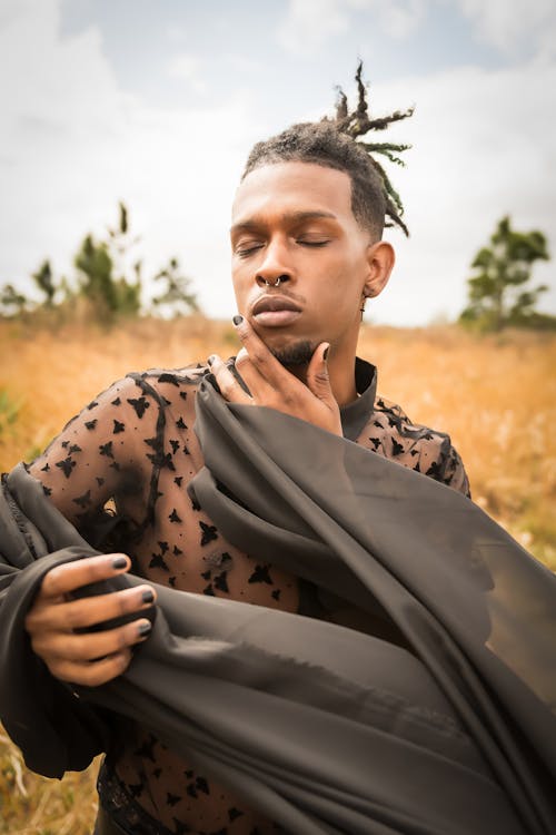 Man with Dreadlocks Wearing a Black Outfit and Posing on a Dry Grass Field 