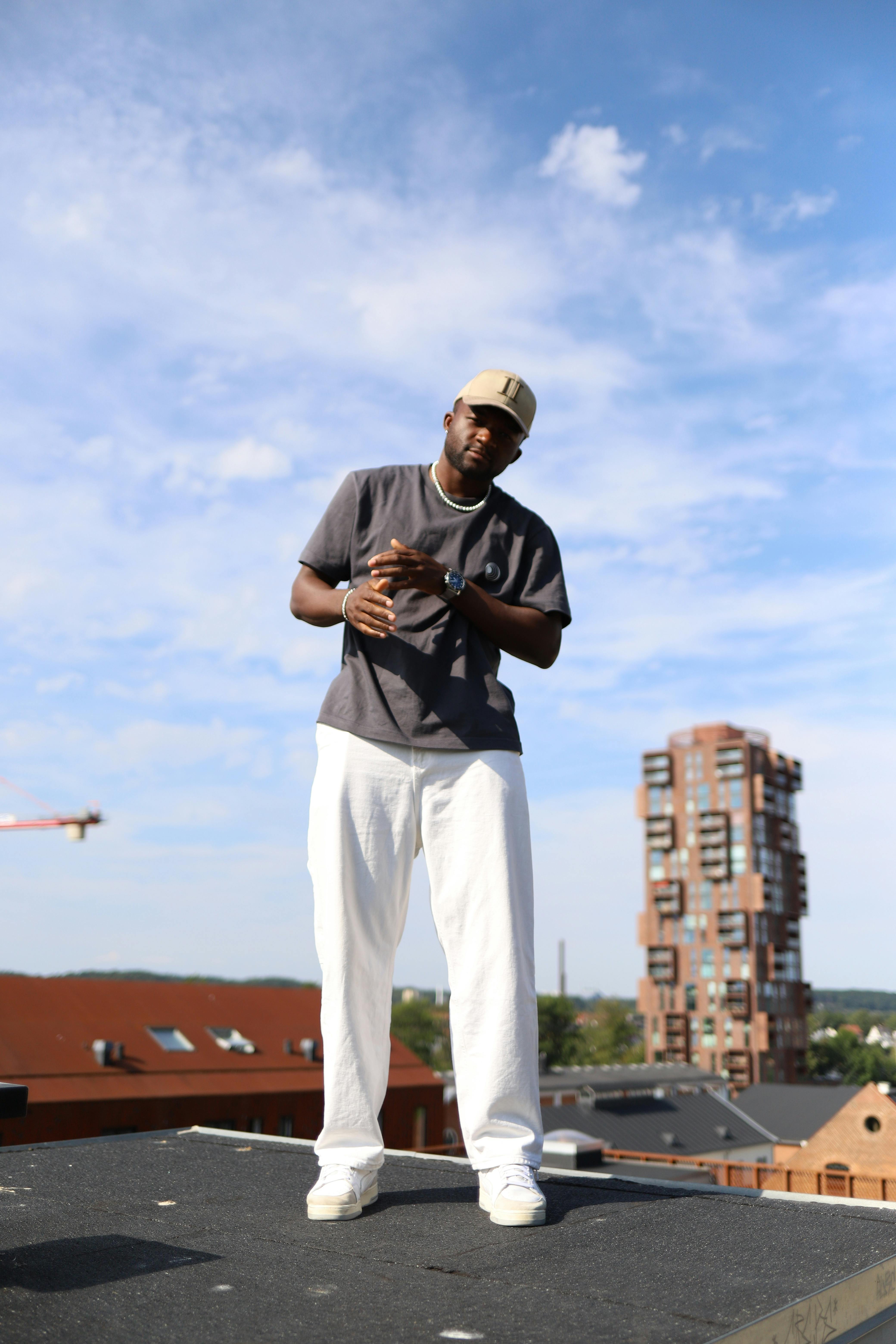 A fashionable man poses on a city rooftop under a clear blue sky, showcasing urban style.