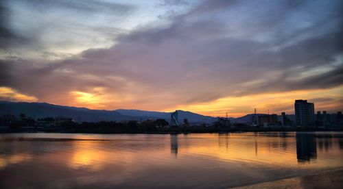 Free Stunning cityscape reflection with colorful sunset sky over calm river. Stock Photo