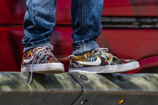Colorful sneakers worn with jeans standing on a metal rail outdoors in sunlight.