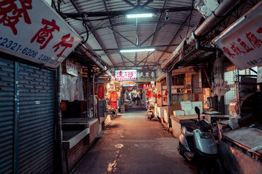 An atmospheric view of an Asian street market at night, with vibrant neon signs and scooters parked along narrow alleys.