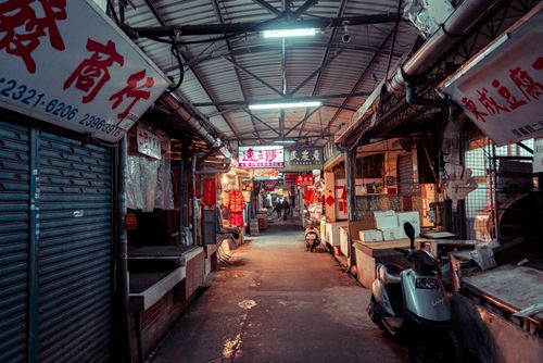 Free An atmospheric view of an Asian street market at night, with vibrant neon signs and scooters parked along narrow alleys. Stock Photo