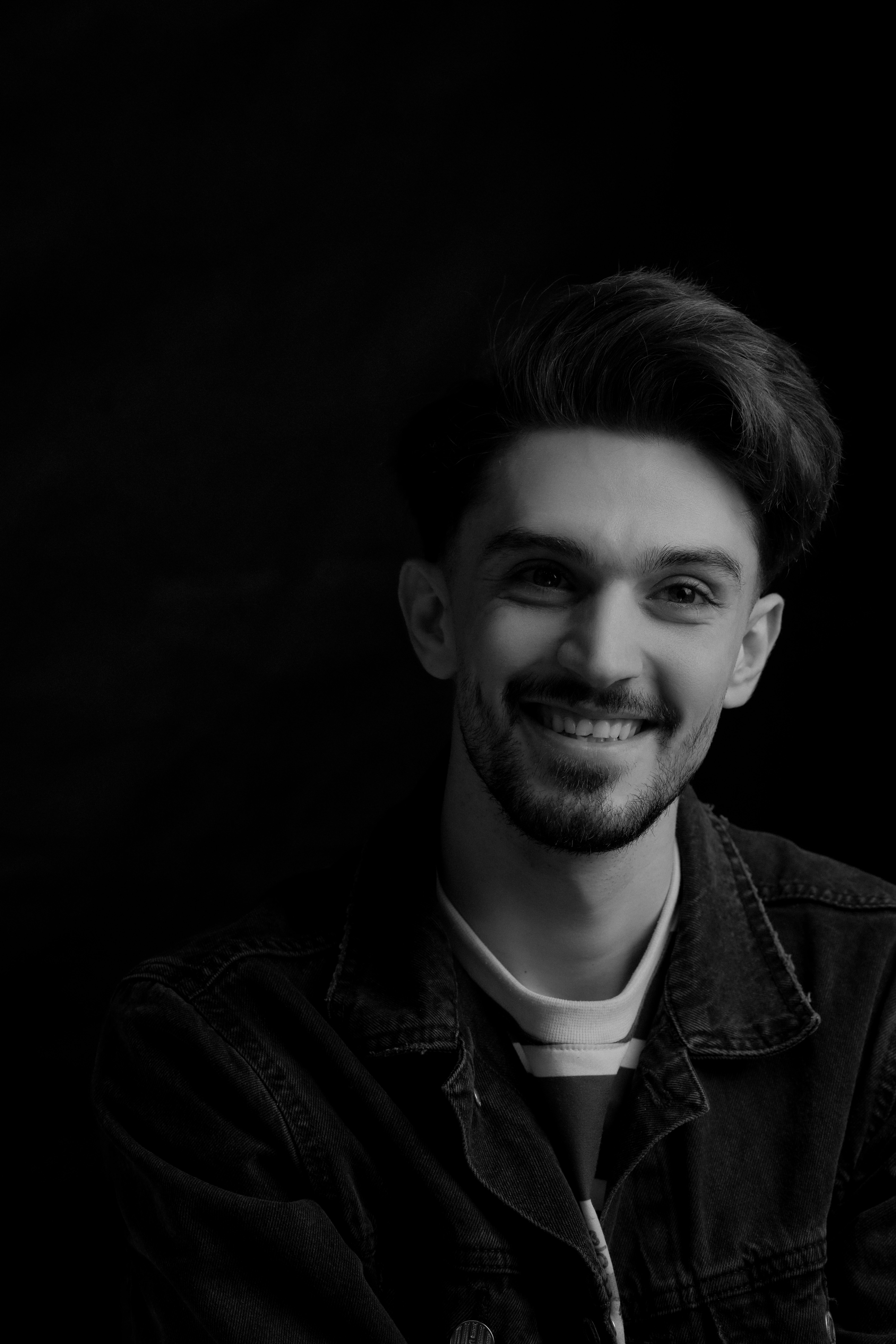 A captivating black and white portrait of a young man with a beard, exuding charm and positivity in a studio setting.