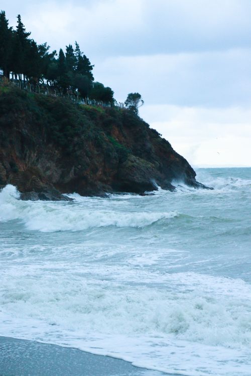 Free Waves crash against a dramatic coastal cliff under a moody sky, capturing nature's power. Stock Photo