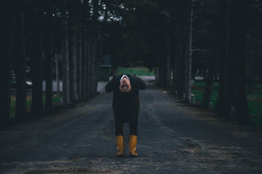 这幅神秘的户外肖像描绘了一个人，他穿着黄色靴子，在幽暗的森林小路上向后弯腰，画面充满了情绪与阴谋