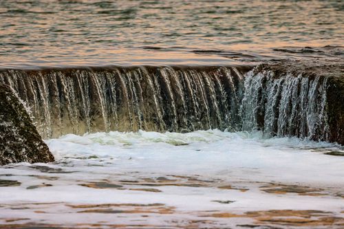 Free Beautiful cascade of water flowing over rocks in a serene natural setting at sunset. Stock Photo