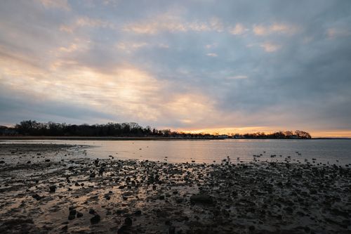 Free A tranquil coastal scene at sunset with a calm sea and rocky shore, capturing serene natural beauty. Stock Photo