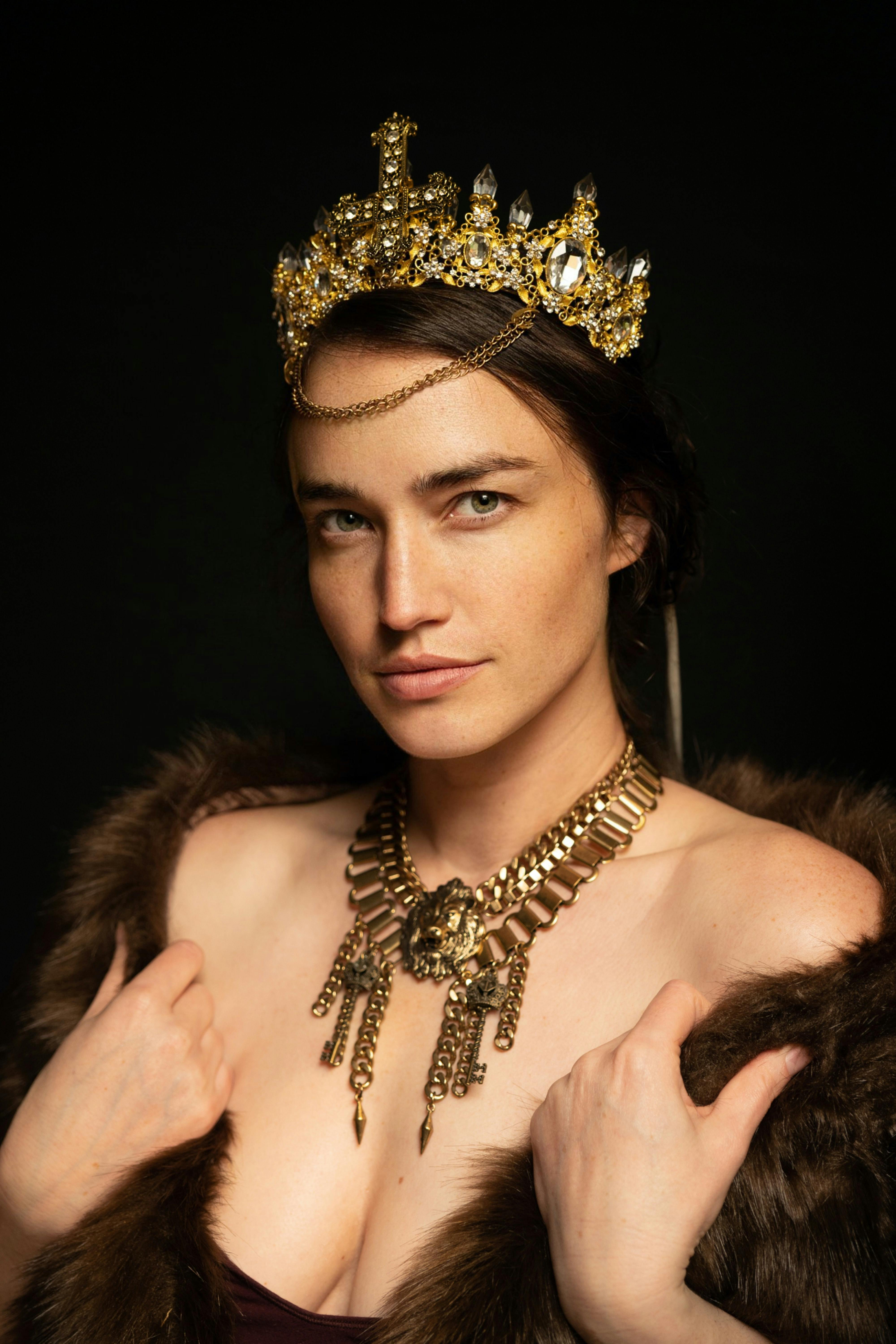 model in medieval gold crown and necklace with a fur scarf on her shoulders