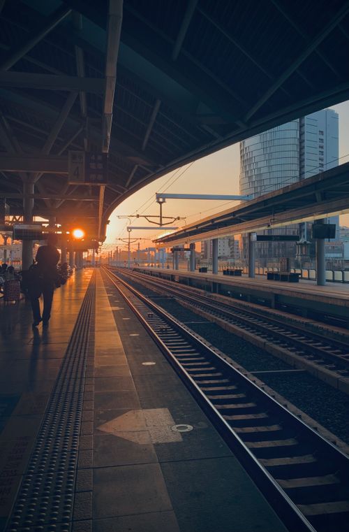 Free Calm evening view of a train station platform during sunset with tracks leading into the distance. Stock Photo