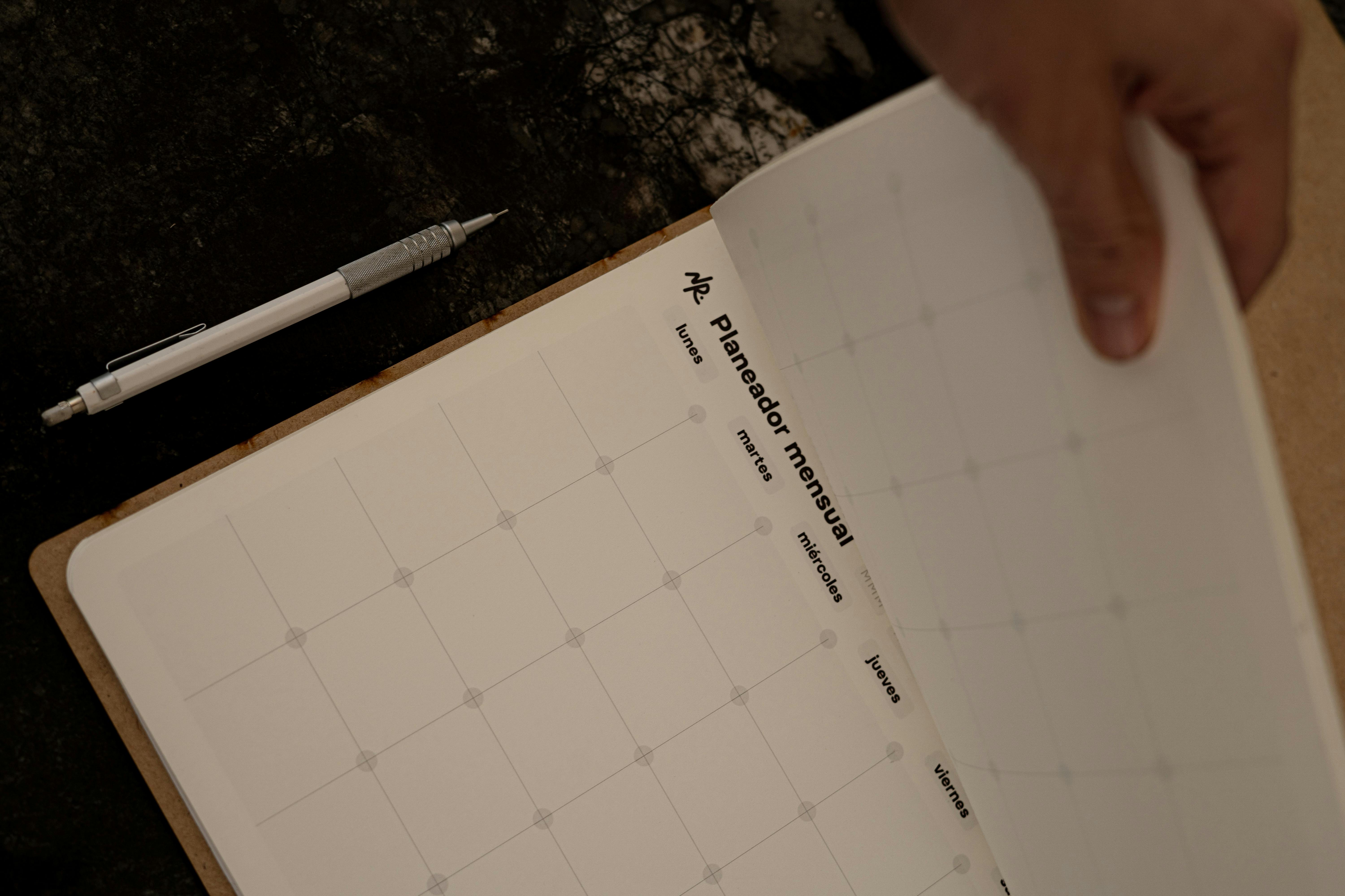 Adult flipping through a monthly planner with pen nearby, emphasizing organization.