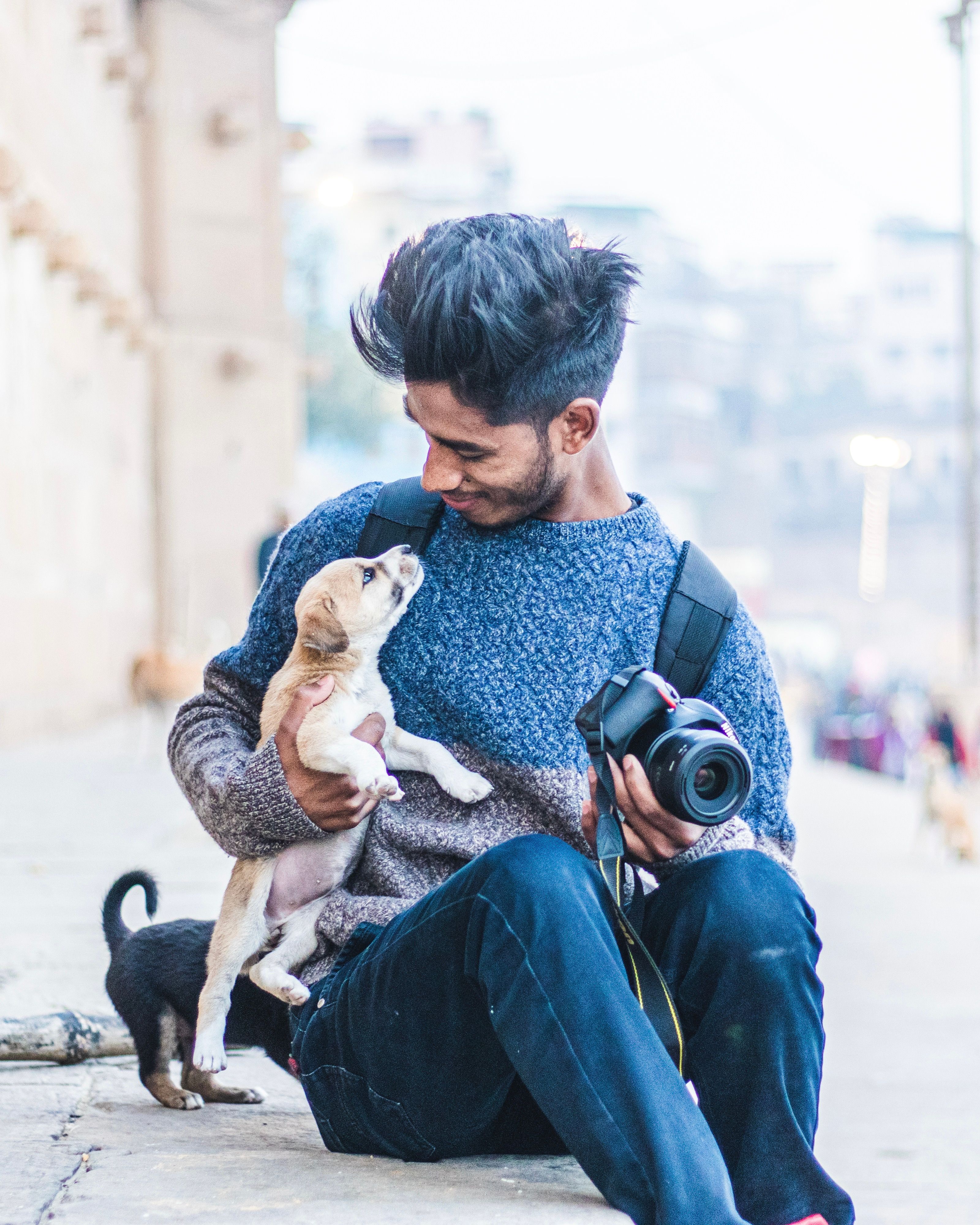A man sitting outdoors with a camera, holding and embracing a puppy.