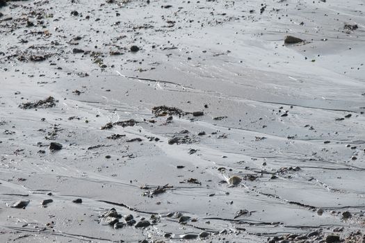 Close-up of wet sand with tidal patterns and scattered pebbles on the beach.