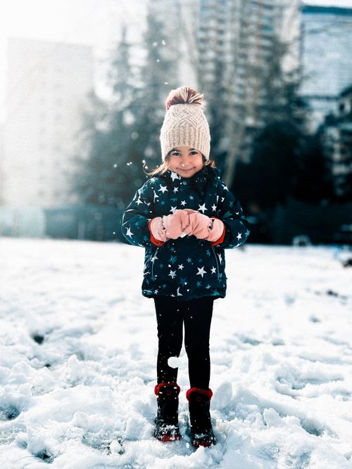 Free A young girl smiles warmly while standing in a snowy park, dressed in star-patterned winter clothing. Stock Photo