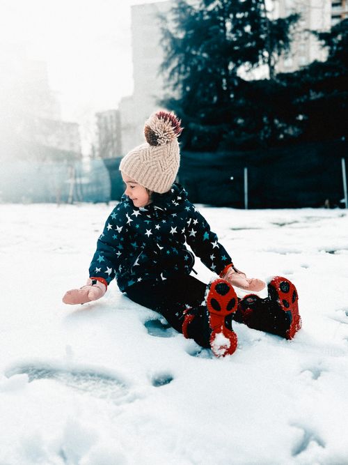 Free A joyful child in warm clothing playing in the snow on a sunny winter day. Stock Photo