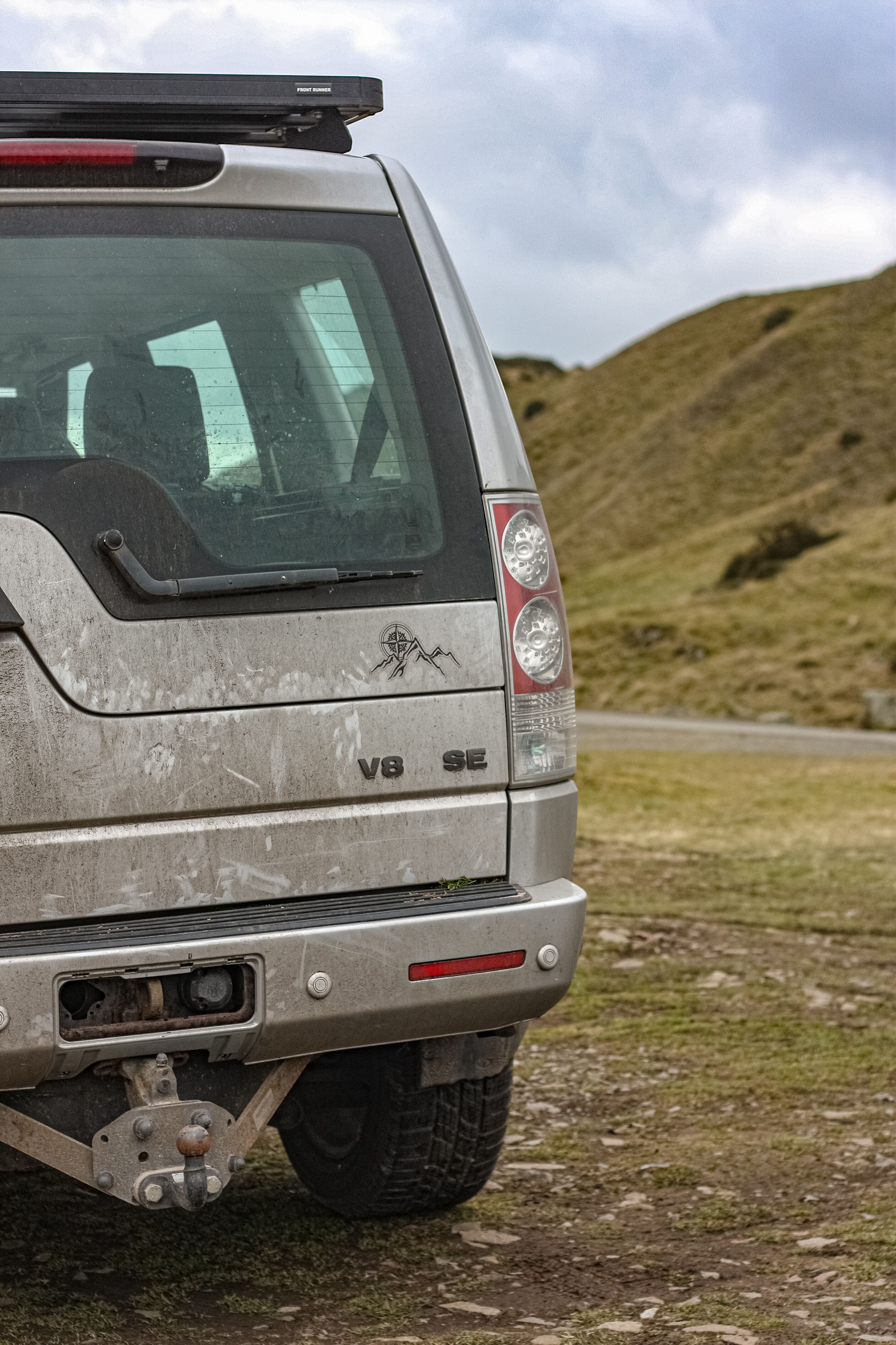 Dirty SUV parked on grassy terrain with overcast skies in the background, showcasing outdoor adventure.