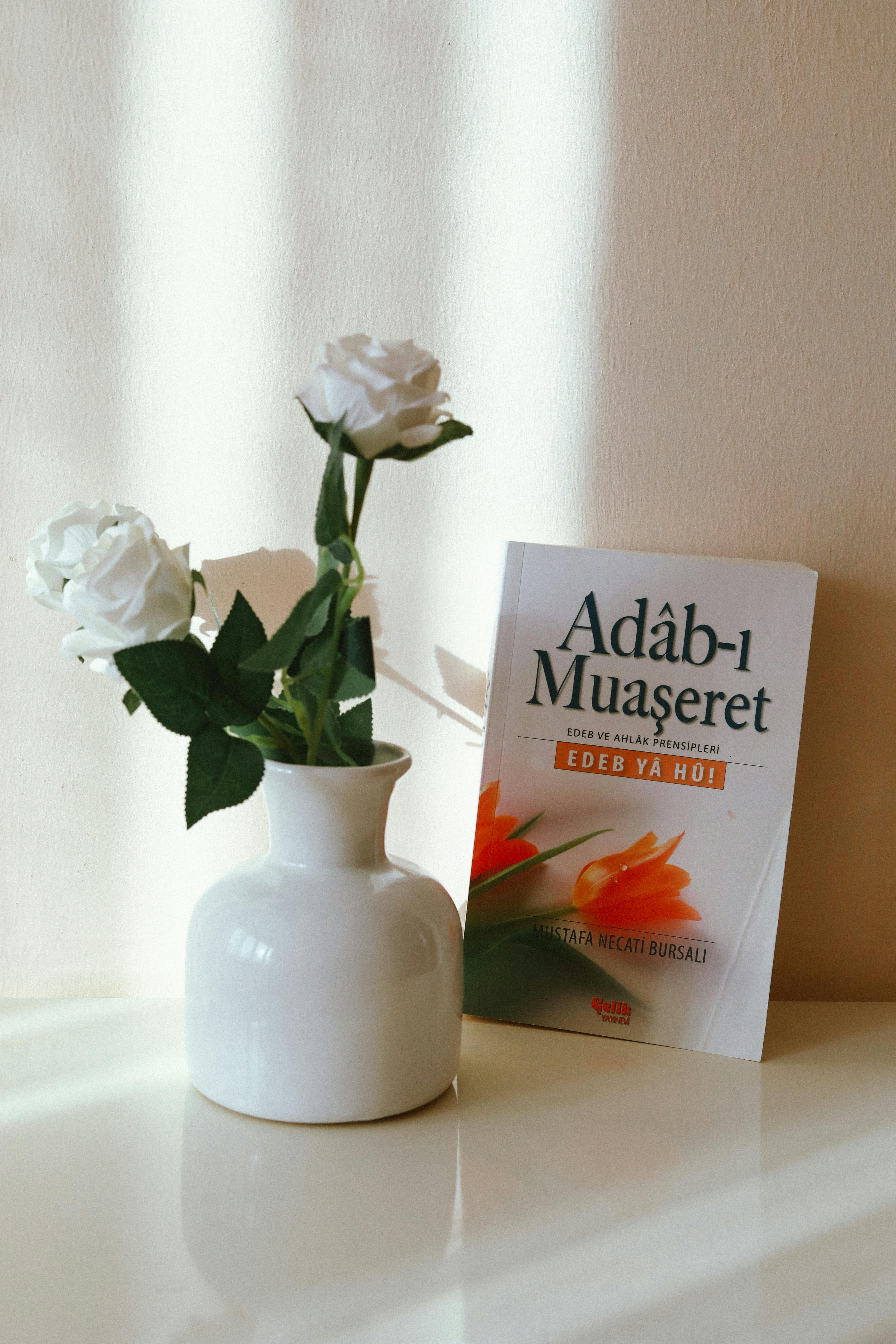 White roses in a ceramic vase beside a book, creating a peaceful interior decoration scene.
