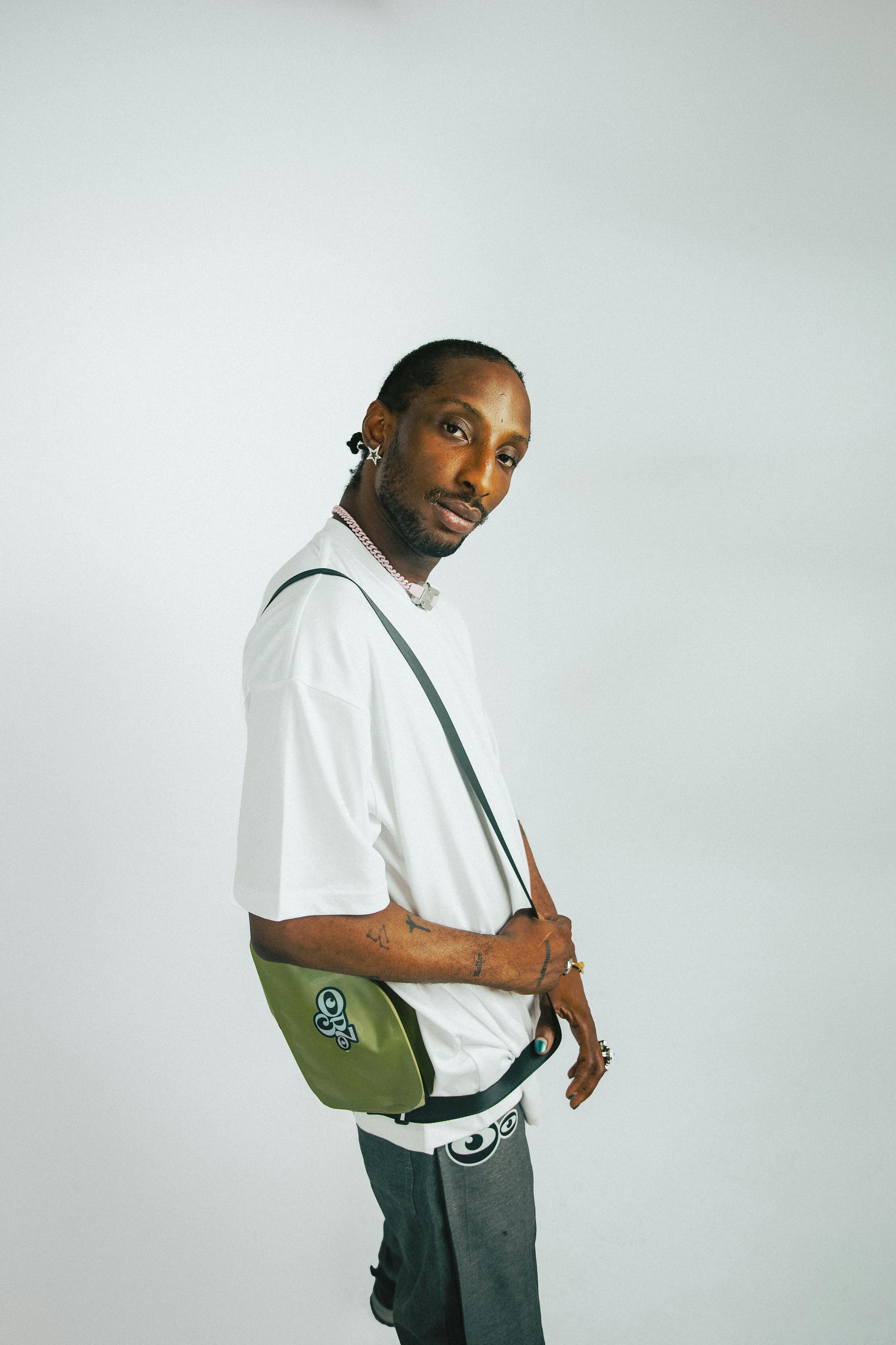Stylish man posing with a green bag and white t-shirt in studio lighting.