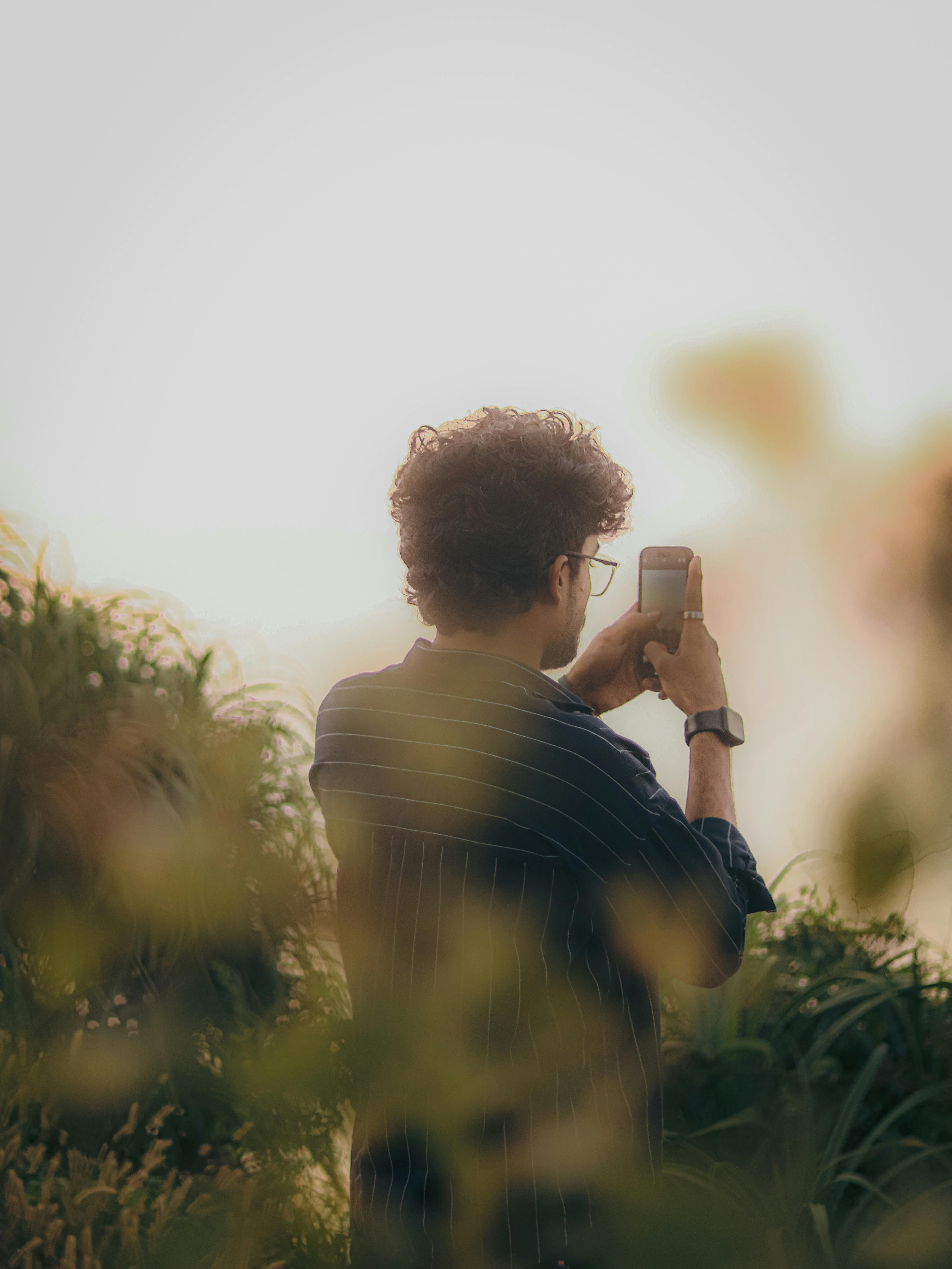 Free A man uses his smartphone to capture the beauty of nature, surrounded by lush greenery. Stock Photo