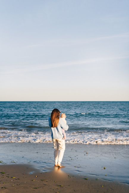Serene moment of a mother holding her baby while watching the ocean waves during a beach vacation.