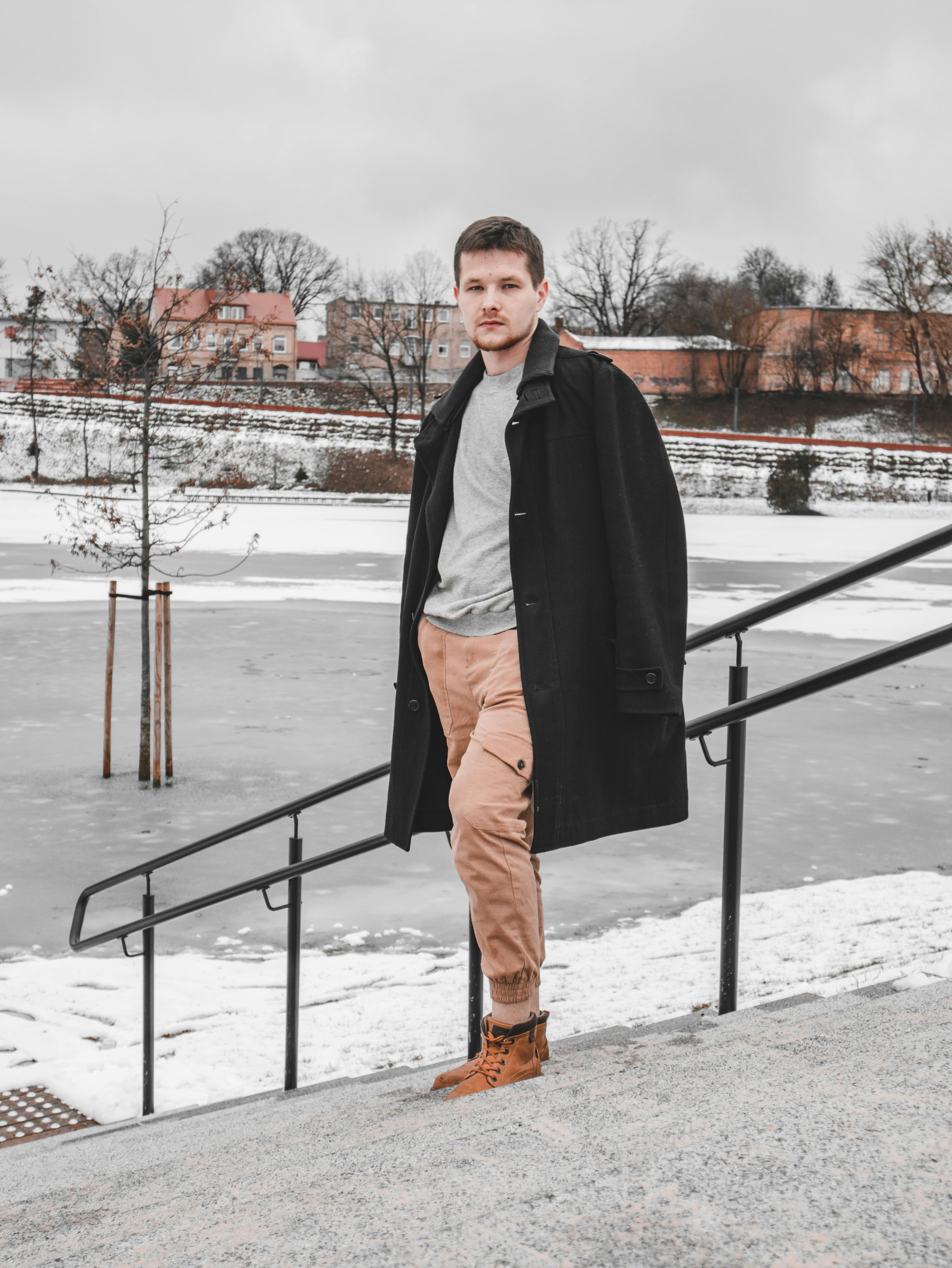 Man wearing a black coat posing outdoors in a snowy winter scene.