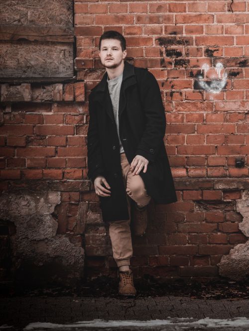 Free Casual portrait of a man leaning on an old red brick wall, exhibiting urban style. Stock Photo