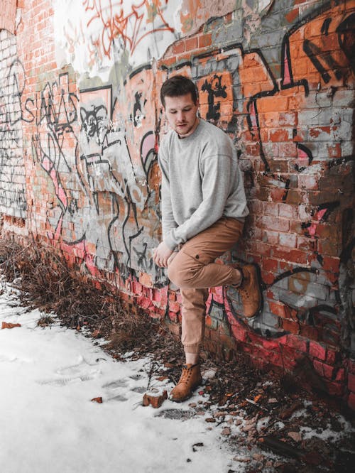 Young Man Leaning on a Brick Wall Covered in Graffiti